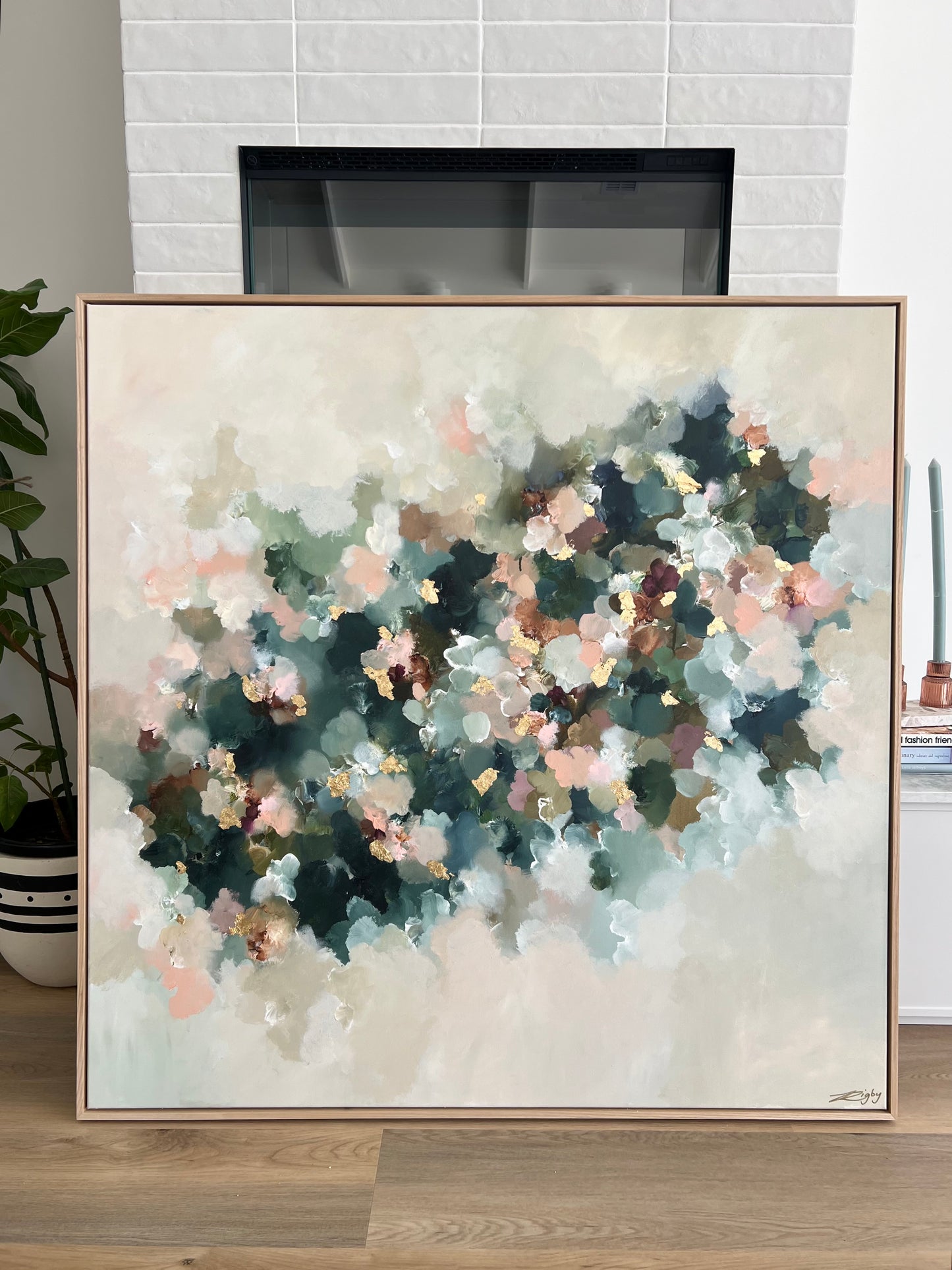 Abstract art piece in a neutral-toned frame on a wooden surface with a fireplace in the background.