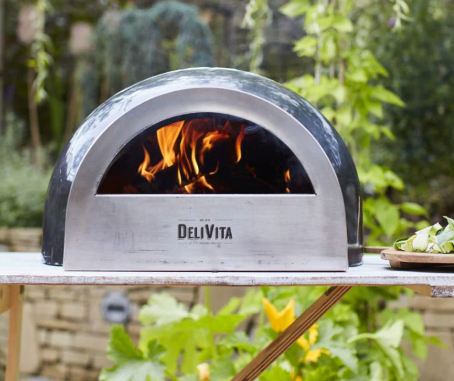Delivita outdoor pizza oven with flames inside on a table outdoors.