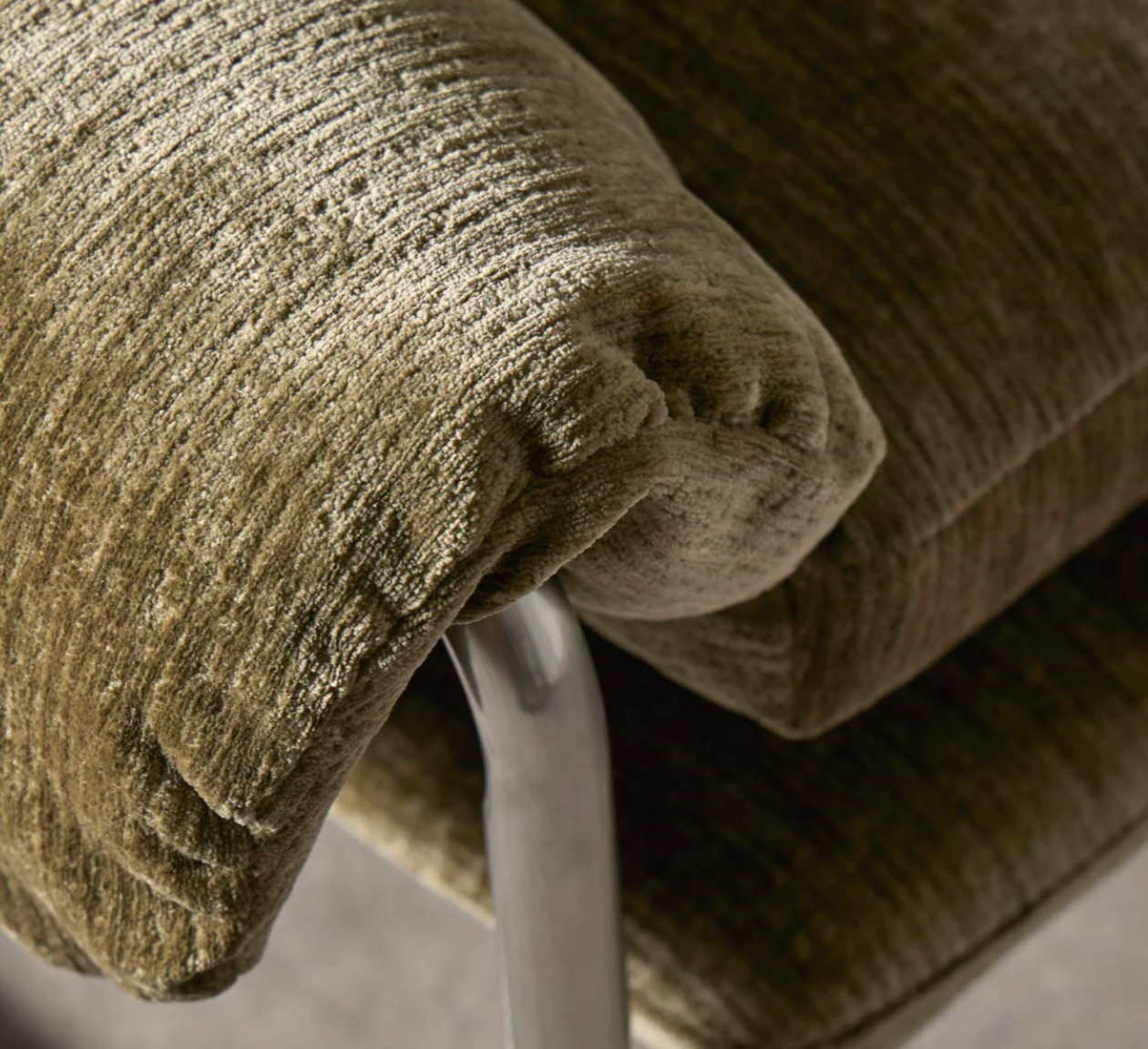 Close-up of a textured upholstered chair cushion in a green fabric, showing the ribbed upholstery and part of a curved metallic support arm.