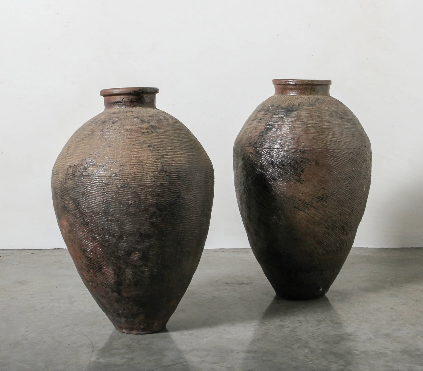 Two large, textured ceramic vases on a gray surface with a white background