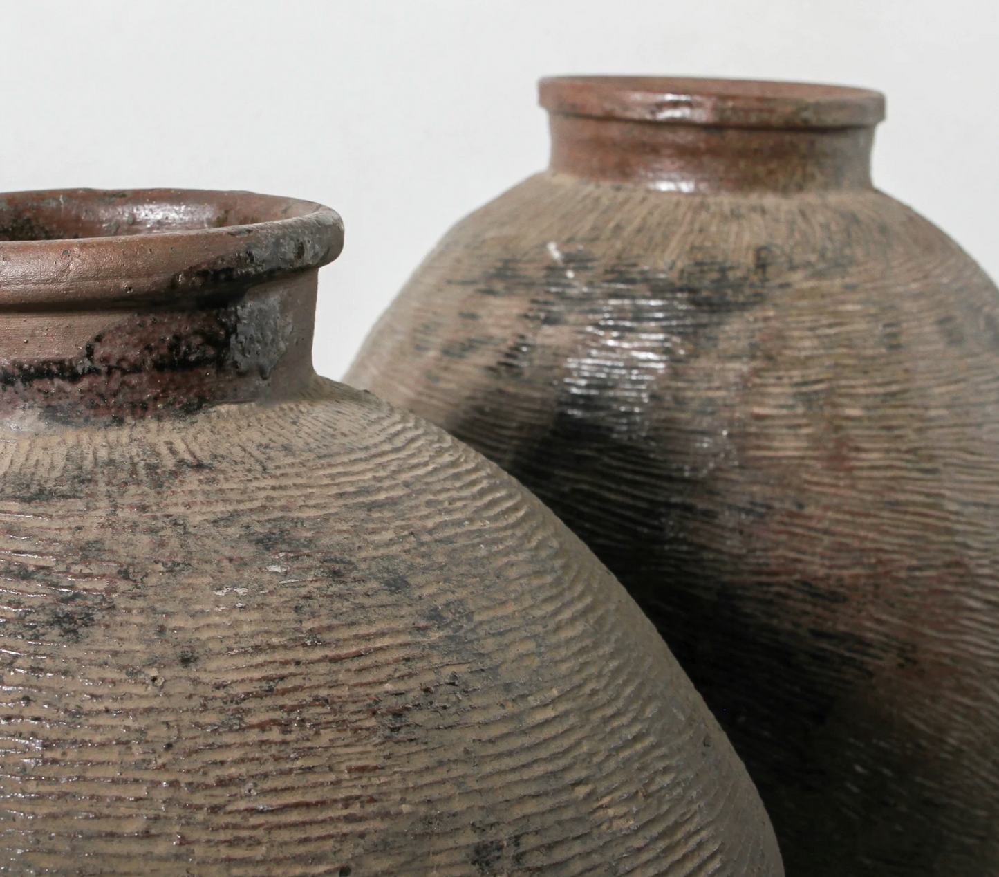 Two brown ceramic pots with textured surfaces on a light gray background