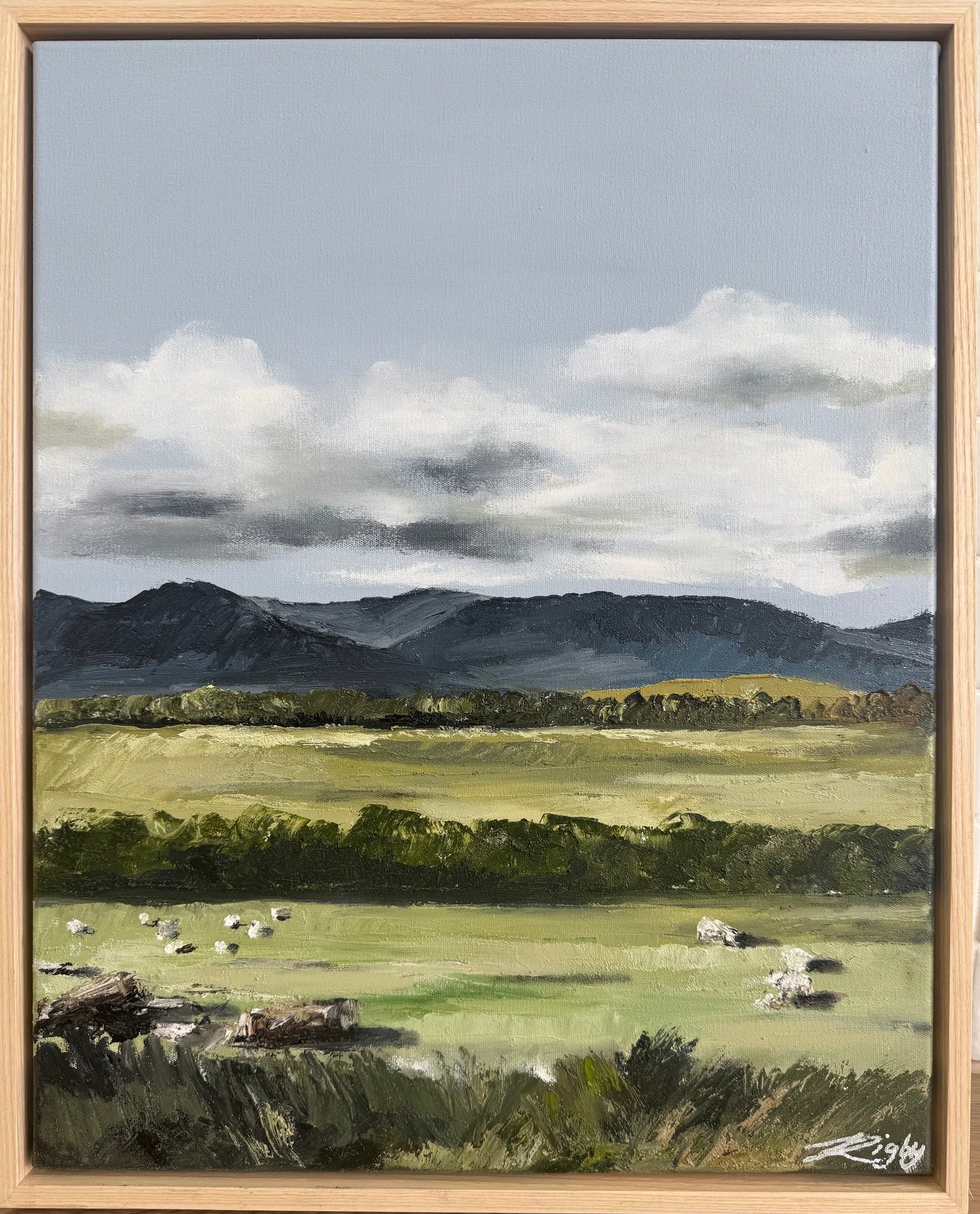 Framed painting of a landscape with mountains, fields, and sheep.
