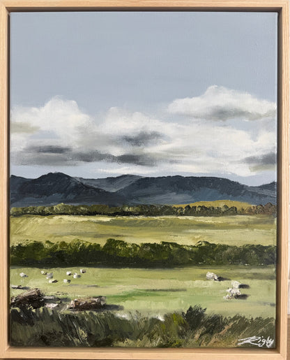 Framed painting of a landscape with mountains, fields, and sheep.