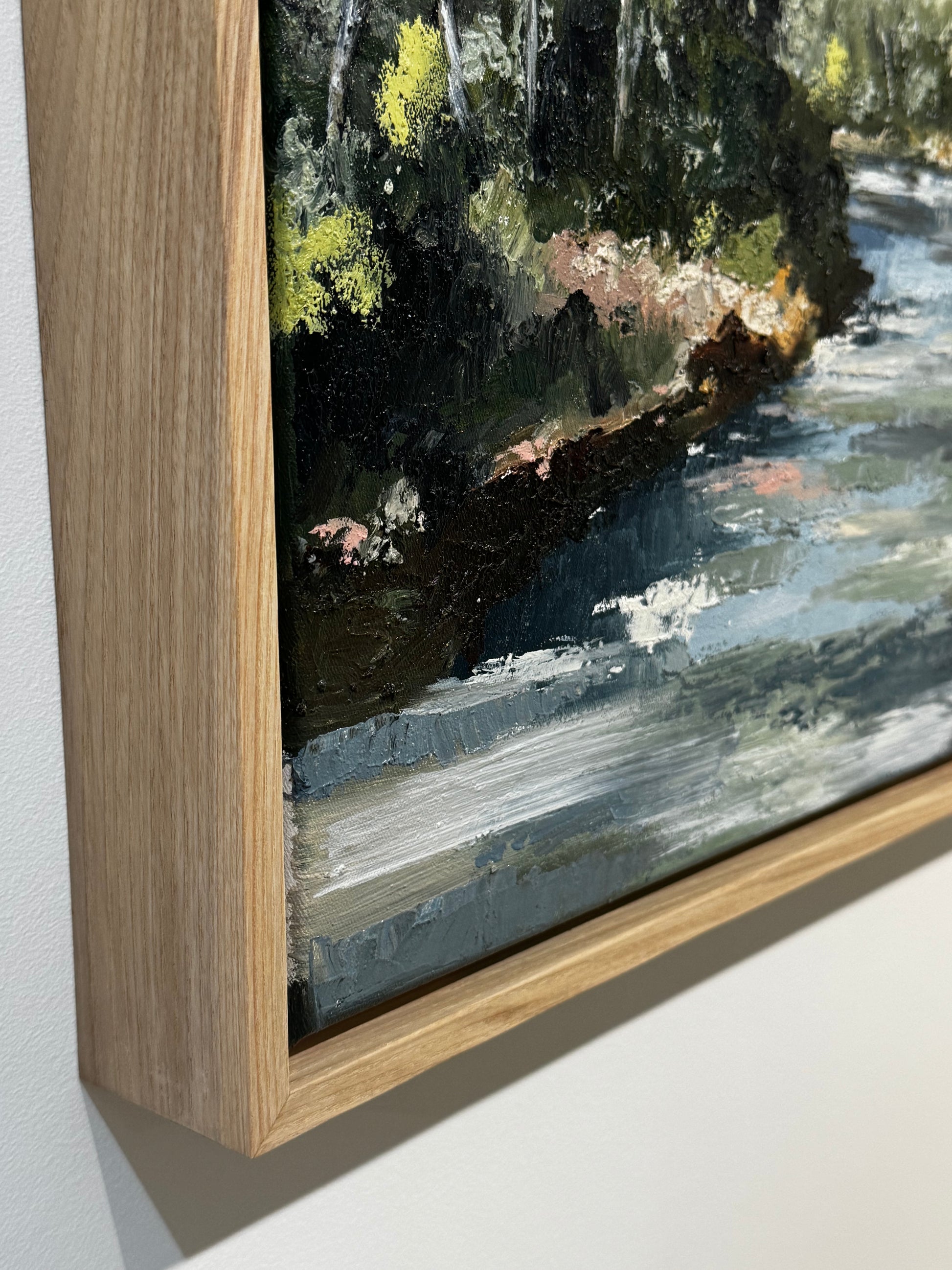 Close-up of a painting with a wooden frame, showing brushstrokes and natural colors.