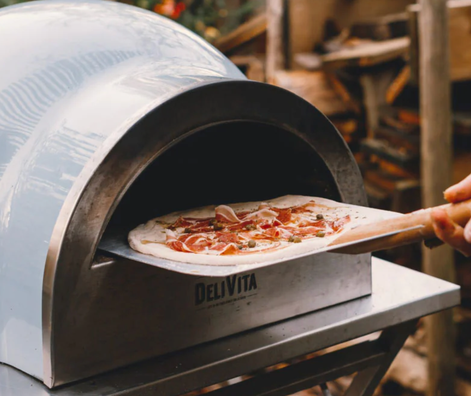 Person placing a pizza into a Delivita outdoor pizza oven.