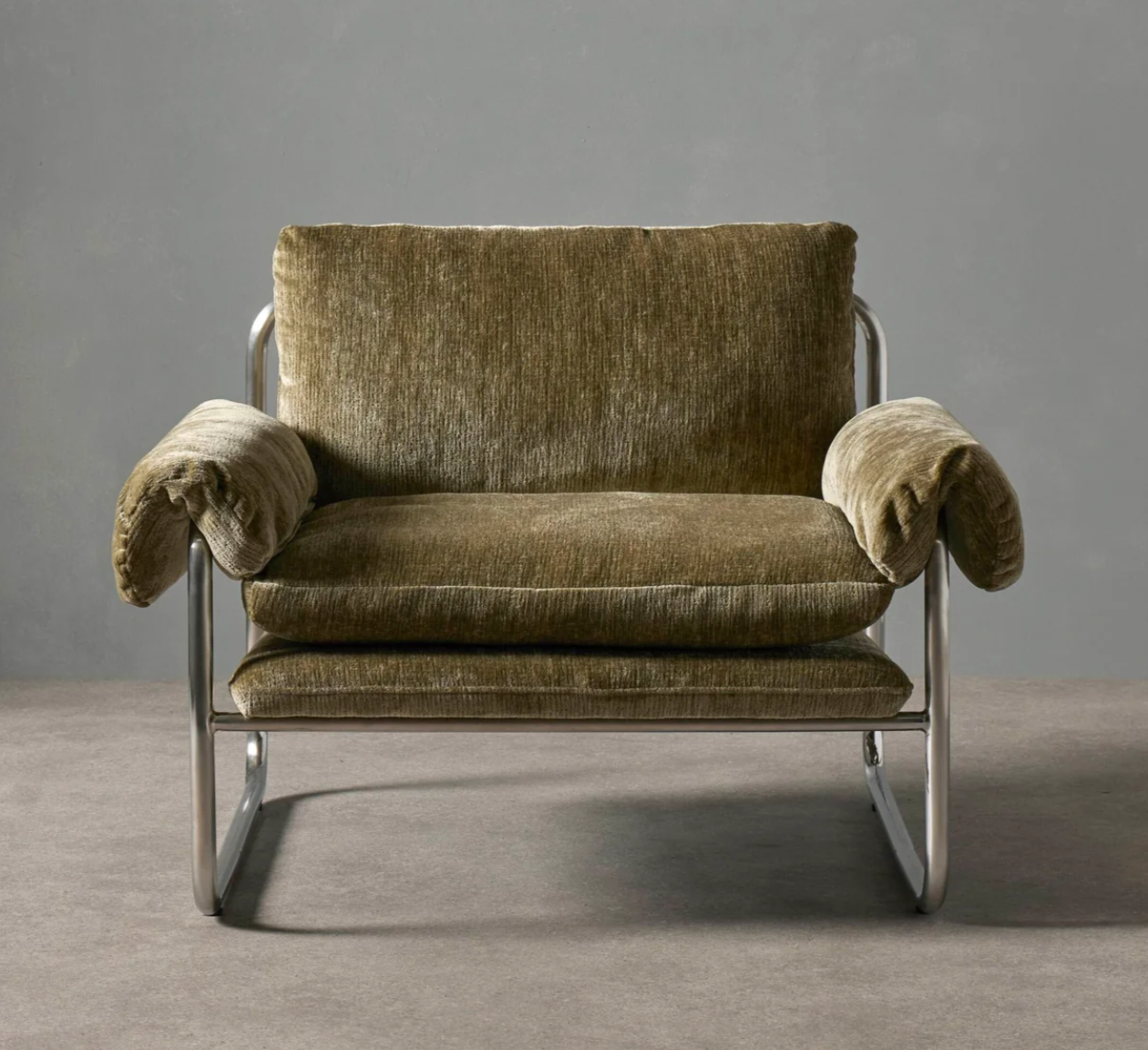 A modern lounge chair with plush olive green velvet cushions and a polished chrome metal frame, set against a neutral gray studio background.