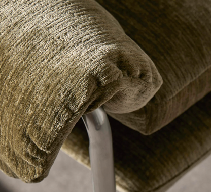 Close-up of a textured upholstered chair cushion in a green fabric, showing the ribbed upholstery and part of a curved metallic support arm.