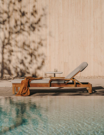 Wooden lounge chair by a pool with a neutral wall and plant in the background