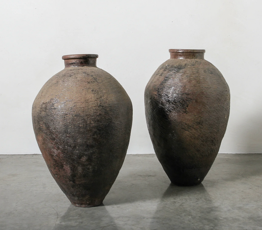 Two large, textured ceramic vases on a gray surface with a white background